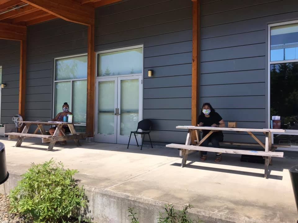 two people sitting outdoors on individual picnic benches that are more than 6 feet apart.