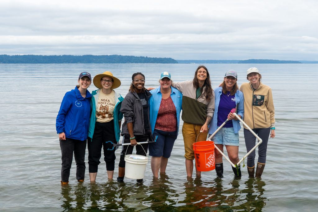 Seven collaborators from NOAA and Washington Sea Grant stand ankle-deep in Puget Sound.