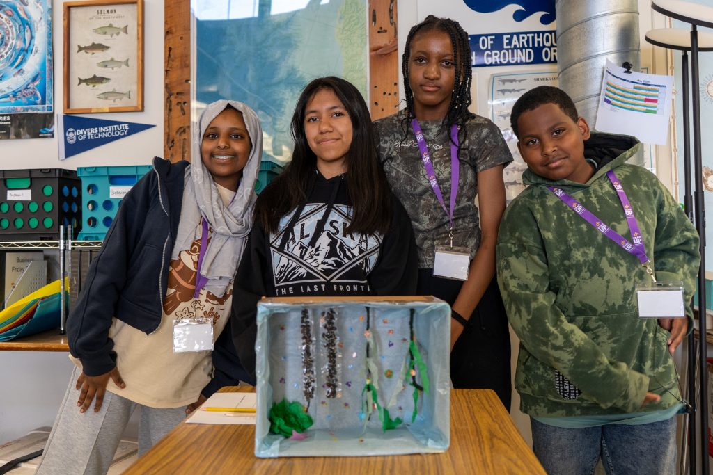 Four students stand behind a diorama of an aquatic scene.