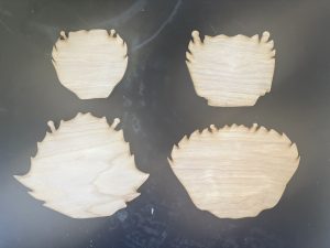 Four flat pieces of wood, laser cut in the shape of the back shells of different crab species, set on a table.