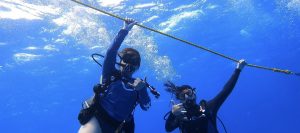 Aina (on the left) and her sister (on the right) in the water with scuba gear holding onto the anchor rope.