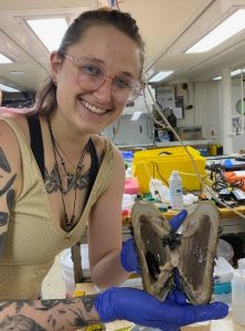 Mel is shown smiling while holding a deep-sea mussel.