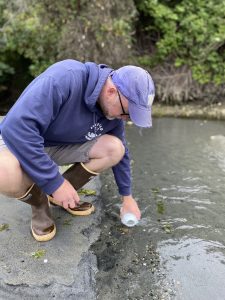 A person leans down to dip a bottle of water in a sandy channel. 