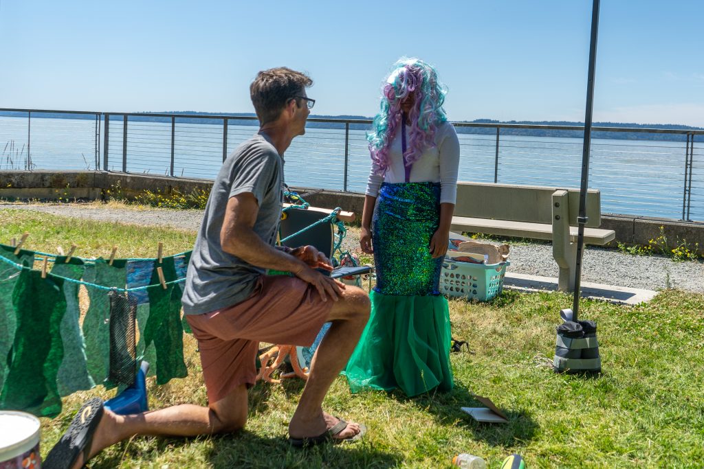 Mike Spranger kneels in front of a student wearing a mermaid wig and costume